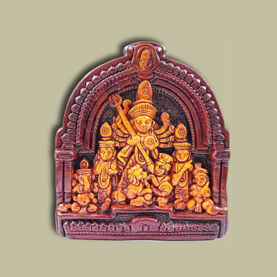 Handcrafted clay idol of Goddess Durga with family in a traditional arched frame, set against a soft beige background.