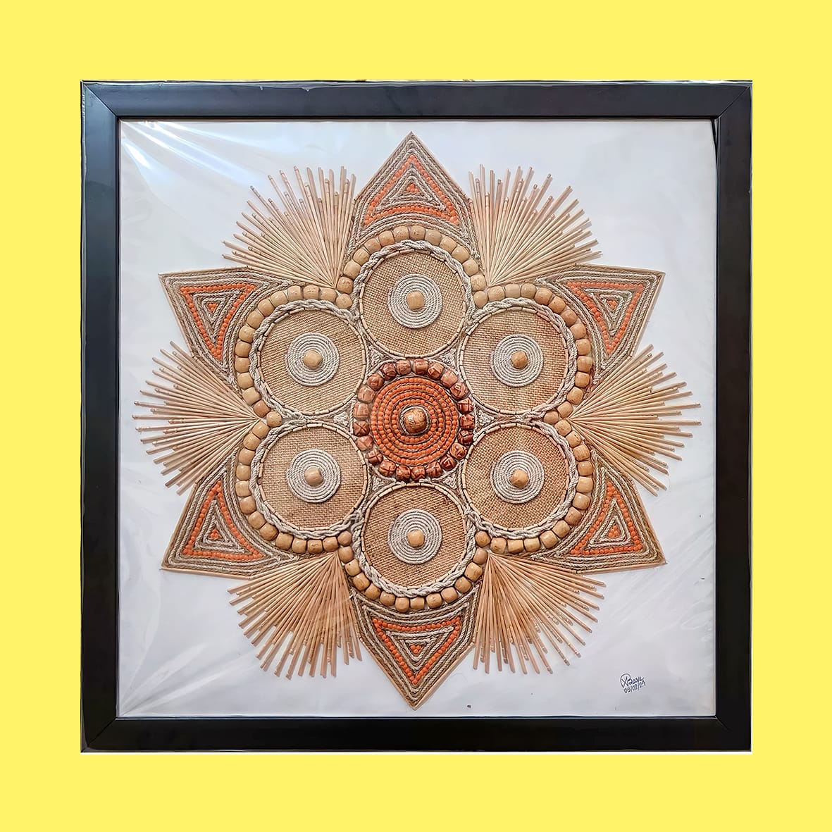 A handcrafted wall hanging featuring circular floral mandala design made with rope, beads, and toothpicks, framed in black over a yellow background.