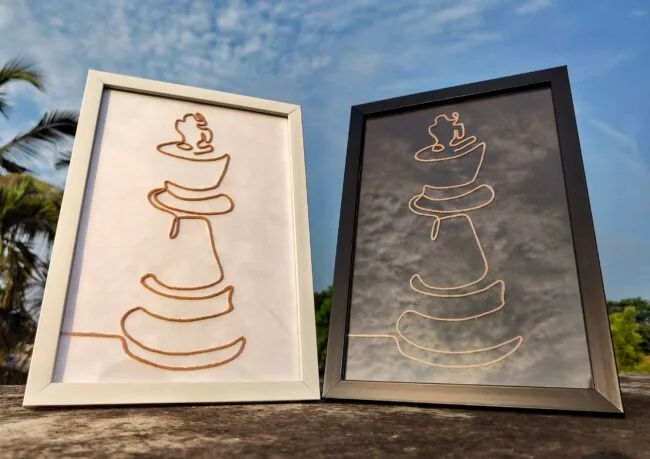 Two handcrafted minimalist rope art portraits depicting abstract representations of a chess king, framed in white and black, displayed outdoors.