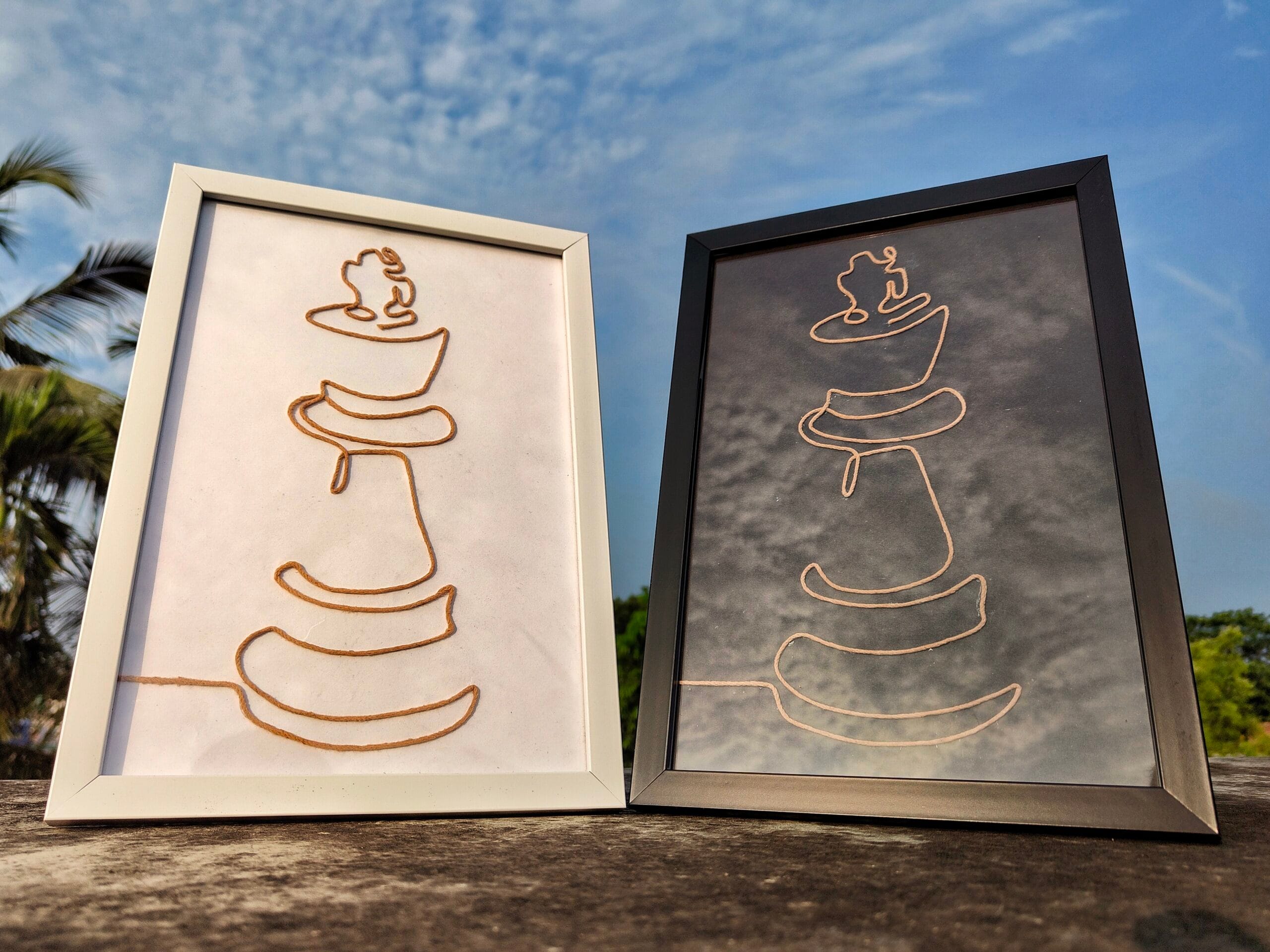 Two handcrafted minimalist rope art portraits depicting abstract representations of a chess king, framed in white and black, displayed outdoors.