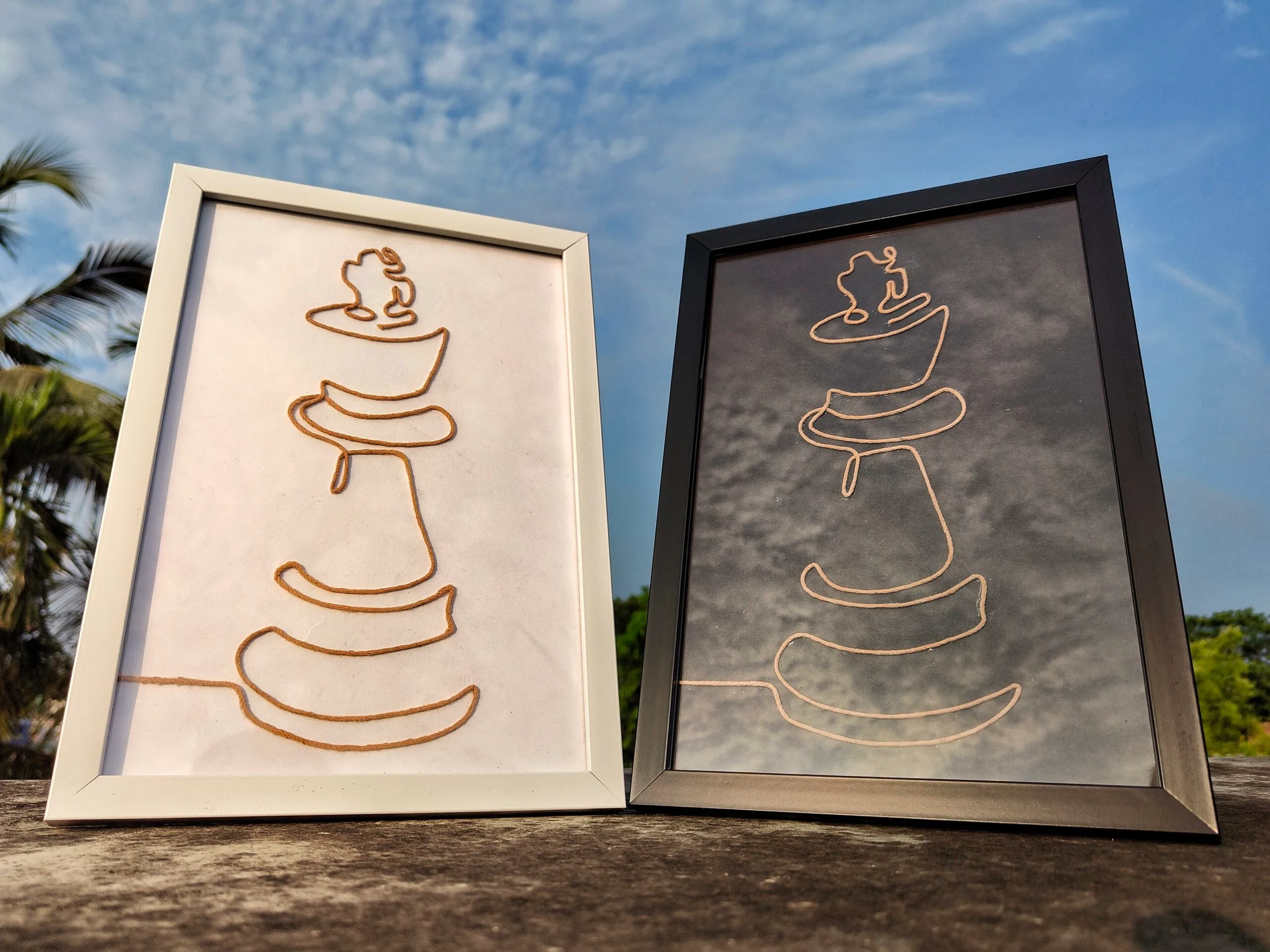 Two handcrafted minimalist rope art portraits depicting abstract representations of a chess king, framed in white and black, displayed outdoors.