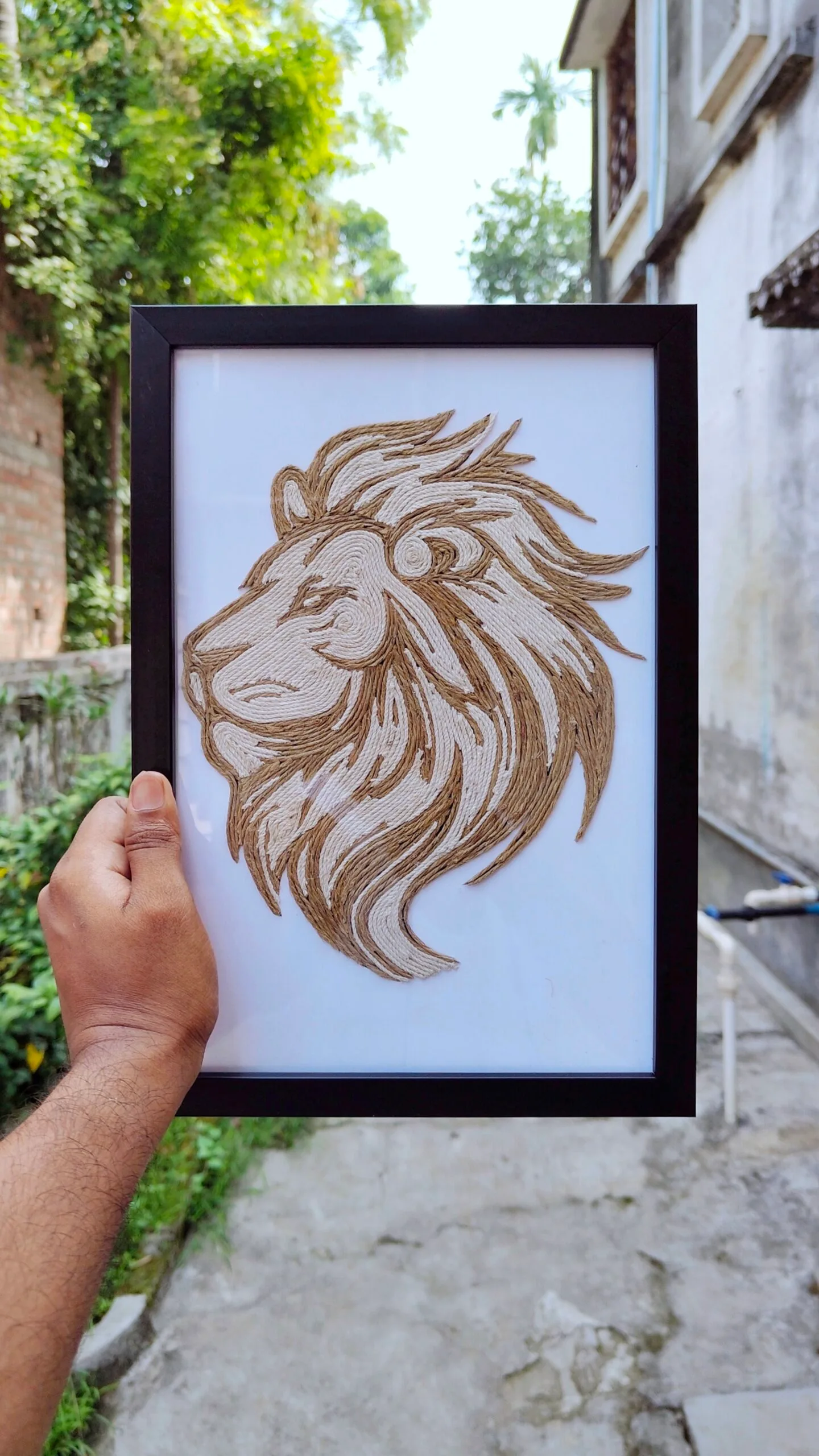 Hand holding a framed rope art of a majestic lion head, crafted with dual-tone jute threads on a white background.