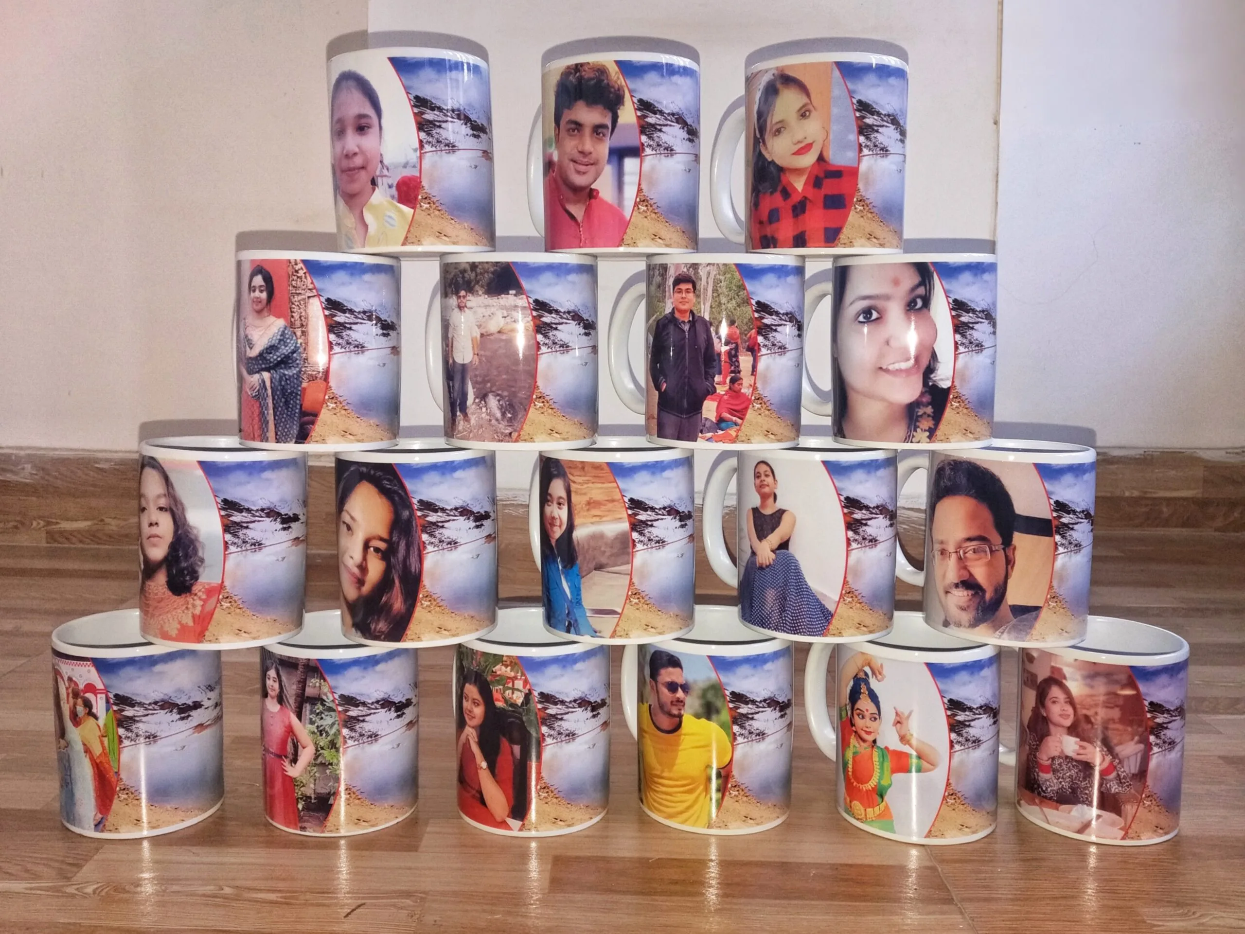 A pyramid stack of custom photo-printed mugs featuring individual portraits on a scenic mountain background, arranged on a wooden floor.