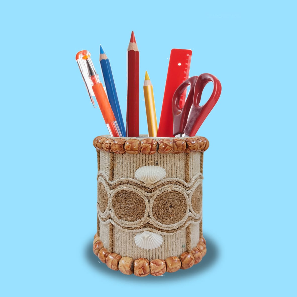 A handcrafted pen stand decorated with rope, shells, and beads, filled with colorful stationery items, against a blue background.