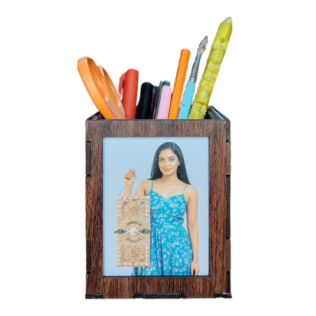 A customized, dark brown MDF wooden pen holder on a white background, filled with colorful pens, a paintbrush, and orange scissors. One side displays a photo of a woman in a blue dress.