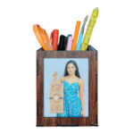 A customized, dark brown MDF wooden pen holder on a white background, filled with colorful pens, a paintbrush, and orange scissors. One side displays a photo of a woman in a blue dress.