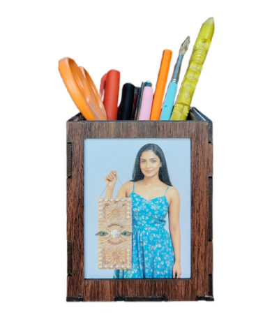 A customized, dark brown MDF wooden pen holder on a white background, filled with colorful pens, a paintbrush, and orange scissors. One side displays a photo of a woman in a blue dress.