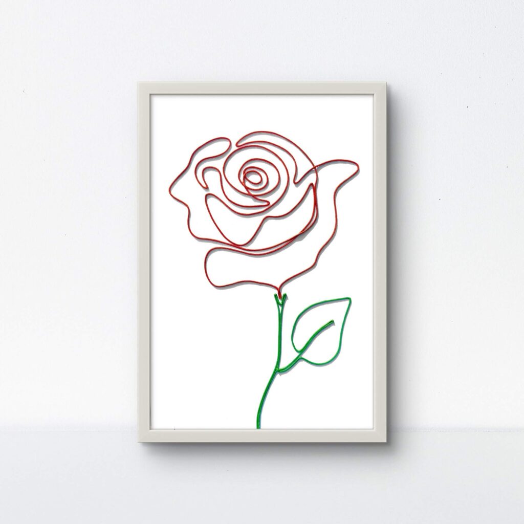 A handcrafted rose made of red and green rope, displayed in a clean white 9"x13" frame on a white background.