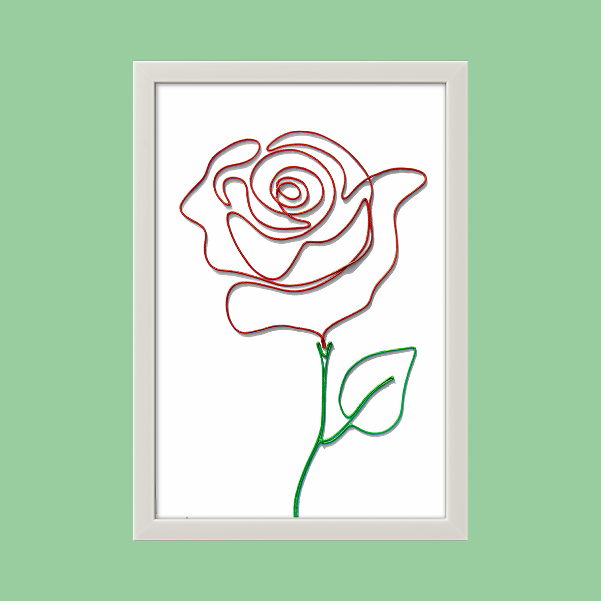 Handcrafted Mixed Colour Rope Art of a blooming red rose with green stem, mounted in an elegant white frame, displayed against a soft green background.