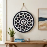 Boho style living room setup with Cowrie and Seashell Mandala Handcrafted Round Wall Decor hanging above a rustic wooden console table next to a potted plant.