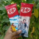 A hand holding two personalized Nestlé KitKat chocolate bars with custom printed photos of women against a blurred green leafy background.