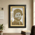 A framed rope craft portrait hanging on a study room wall next to a calendar, with a desk, books, and a indoor plant visible in the foreground.