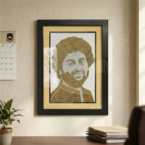 A framed rope craft portrait hanging on a study room wall next to a calendar, with a desk, books, and a indoor plant visible in the foreground.