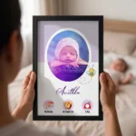 Close up real life shot of hands holding upahar18 personalized baby birth details classic photo frame design 016 with a blurred newborn baby sleeping in bed in the background