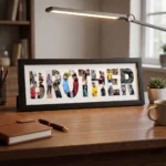 A black rectangular Upahar18 Brother Photo Frame displaying a custom photo collage inside the word BROTHER, neatly placed on a wooden study table next to a notebook, pen, and desk lamp.