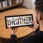 An over-the-shoulder view of a person holding a black rectangular Upahar18 Brother Photo Frame featuring a custom picture collage inside the bold text BROTHER, with a wooden table in the background.
