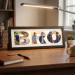 A classic black rectangular Upahar18 Brother Photo Frame displaying a custom photo collage inside the word BRO, neatly placed on a wooden desk next to a pen, notebook, and desk lamp.