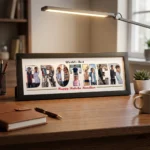 A classic black rectangular Upahar18 Brother Photo Frame with a custom photo collage inside the word BROTHER and Rakhi text, sitting on a wooden desk next to a pen, notebook, and desk lamp.