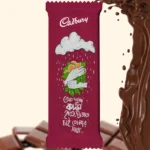 A customized maroon Cadbury Dairy Milk chocolate wrapper with the Cadbury logo, an illustration of hands holding Kadam flowers in the rain, and Bengali text, placed next to a splash of liquid chocolate.