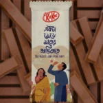 A customized beige KitKat chocolate wrapper featuring the Nestlé KitKat logo, romantic Bengali typography, and an illustration of a couple playing with soap bubbles, set against a background of KitKat chocolate fingers.