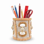 Studio shot of Upahar18 Handmade Eco-Friendly Rope Base Pen Stand on a clean white background. The desk organiser holds colorful pencils, a red ruler, and scissors, highlighting the intricate detail of the woven rope structure, cowrie shells, and delicate bamboo trims.