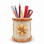 Studio shot on a pure white background of Upahar18 Handmade Eco-Friendly Rope Base Pen Stand filled with colourful writing utensils, scissors, and a red ruler, highlighting its vibrant red bead floral patterns, vertical jute lines, and sparkling mirror work.
