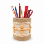 Studio shot on a white background of Upahar18 Handmade Eco-Friendly Rope Base Pen Stand filled with office stationery. The image highlights the detailed horizontal rows of mini bamboo beads framing a central pattern of cream rope and smooth wooden seed flowers.