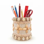 Studio shot of Upahar18 Handmade Eco-Friendly Rope Base Pen Stand with Cowrie Shell borders against a white background. This artisanal desk organiser is filled with pencils, pens, and scissors, highlighting the polished cowrie shells lining the top and bottom rims along with a central wooden seed flower pattern.