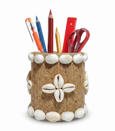 Studio shot of Upahar18 Handmade Eco-Friendly Rope Base Pen Stand against a clean white background. This rustic desk organiser features a natural brown coir rope body decorated with white seashells on the rims and a central four-petal cowrie shell floral motif, filled with pens, pencils, a ruler, and scissors.