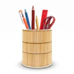 An isolated studio shot of a round handmade pen holder by Upahar18 on a plain white background. The holder is wrapped in brightly colored green, yellow, pink, and blue wooden sticks, filled with office stationery including pencils, a pen, and a pair of scissors.
