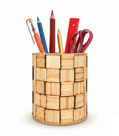 A front-facing studio shot of the Upahar18 handmade pen holder over a solid white background. The holder showcases a textured basket-weave look created with light tan wooden sticks, filled with various office stationery items like color pencils and scissors.