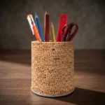 A front view studio shot of the Upahar18 handmade pen holder over a clean white background. The cylinder stand showcases an intricate basket-weave texture made of tiny light-brown natural elements, filled with basic stationary like pencils, a red ruler, and maroon scissors.