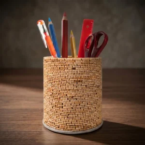 A front view studio shot of the Upahar18 handmade pen holder over a clean white background. The cylinder stand showcases an intricate basket-weave texture made of tiny light-brown natural elements, filled with basic stationary like pencils, a red ruler, and maroon scissors.