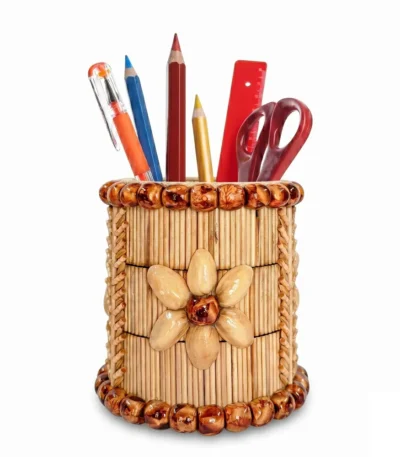 Alt Text: An isolated product shot of the Upahar18 handmade pen stand against a plain white background. The cylindrical holder features an artistic flower motif made from pistachio shells, vertical columns of thin natural wooden sticks, and prominent horizontal rings of polished brown wooden beads decorating both the top and bottom rims. It contains colored pencils, a ruler, and scissors.