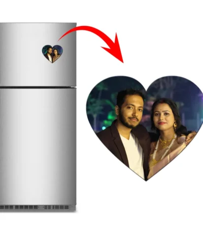A product graphic showing a vertical stainless steel refrigerator on the left with a heart-shaped custom flexible photo magnet attached to the door. A big red arrow curves toward a large view of the heart magnet on the right, which features a personalized wedding or anniversary photo of an Indian couple smiling together at night by upahar18.