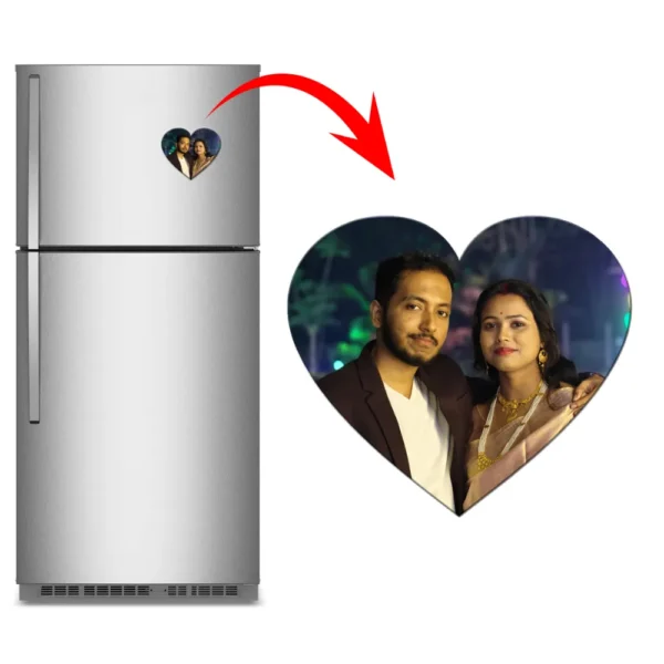 A product graphic showing a vertical stainless steel refrigerator on the left with a heart-shaped custom flexible photo magnet attached to the door. A big red arrow curves toward a large view of the heart magnet on the right, which features a personalized wedding or anniversary photo of an Indian couple smiling together at night by upahar18.