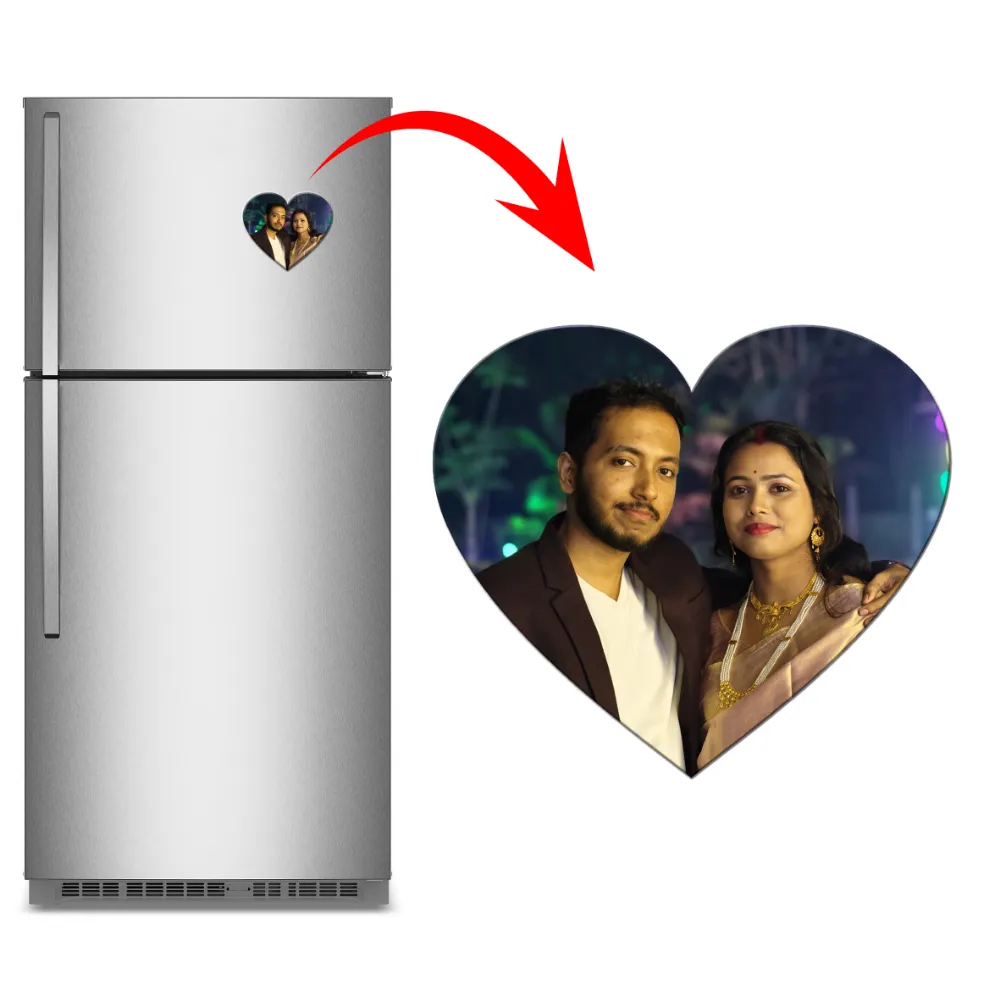 A product graphic showing a vertical stainless steel refrigerator on the left with a heart-shaped custom flexible photo magnet attached to the door. A big red arrow curves toward a large view of the heart magnet on the right, which features a personalized wedding or anniversary photo of an Indian couple smiling together at night by upahar18.