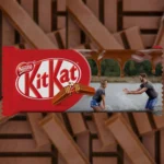 A horizontally designed upahar18 customized red kitkat chocolate bar package featuring a personalized photo printed image of a couple playing in the water next to a melted chocolate stream.