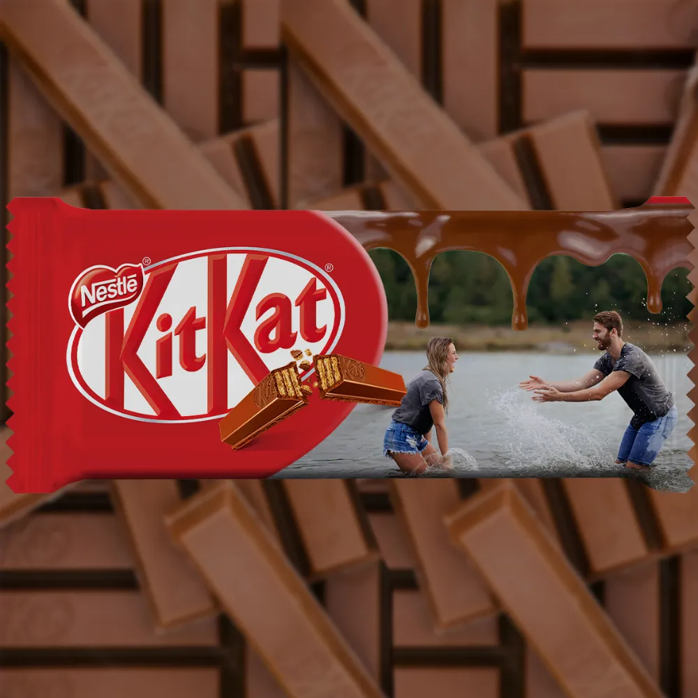 A horizontally designed upahar18 customized red kitkat chocolate bar package featuring a personalized photo printed image of a couple playing in the water next to a melted chocolate stream.