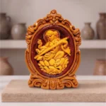 Designer framed Terracotta Maa Saraswati idol by upahar18 displayed elegantly on a wooden slab inside a minimalist decor studio backdrop, crafted in Krishnanagar.