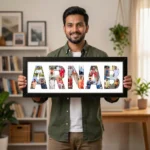 A smiling young man standing in a living room and holding a large classic black rectangular Upahar18 NAME Photo Frame displaying a custom-printed photo collage inside the name ARNAB on a white background.