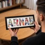 An over-the-shoulder view of a person holding a classic black rectangular Upahar18 NAME Photo Frame that showcases a high-quality custom print of the name ARNAB filled with a colorful photo collage, with a wooden table in the background.