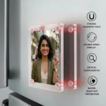 An infographic image showing a side-angle view of a rectangular crystal-clear acrylic magnetic photo frame attached to a silver refrigerator door, displaying a personalized photo of a smiling woman in a green jacket. The double-sided frame is shown slightly pulled apart to highlight its strong corner magnets glowing with a subtle red light effect, accompanied by text icons on the right detailing features like strong magnetic hold, double-sided display, crystal clear acrylic, and water-resistant protection by upahar18.