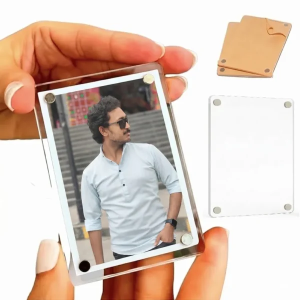 A close-up view of a hand holding a vertical rectangle-shaped personalized acrylic magnetic fridge magnet frame containing a photo of a man in sunglasses, with a separate blank clear block and a brown paper covered piece in the background by upahar18.