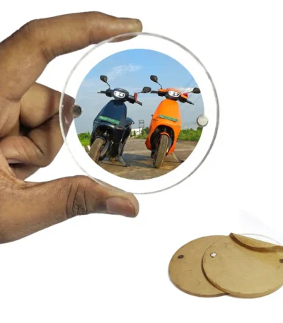 A hand holding a circular round-shaped clear acrylic magnetic frame featuring a personalized photo of two modern electric scooters on a sunny road, next to two unpeeled brown paper heart sheets by upahar18.