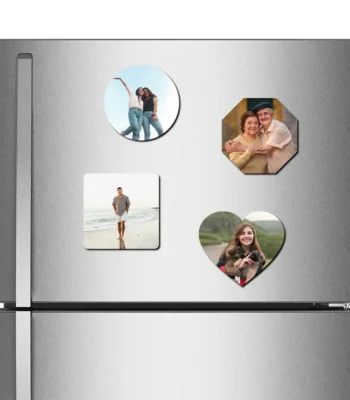 A straight front view of a stainless steel refrigerator door decorated with a combo set of four different shaped custom MDF photo fridge magnets, featuring a round magnet with two women, an octagon magnet with an elderly couple, a square magnet with a man on a beach, and a heart-shaped magnet with a woman and puppies, all printed with vibrant personalized photos by upahar18.