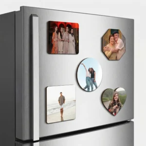 A close-up side angle view of a metallic double-door refrigerator highlighting a combo set of five different shaped personalized MDF photo printed fridge magnets, displaying the clean layered dark wooden edge profiles of the rectangle, octagon, round, square, and heart shapes against the brushed steel finish by upahar18.