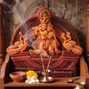 Handcrafted upahar18 Terracotta Radha Krishna idol illuminated in a home mandir setup with incense smoke, marigold flowers, and a traditional clay diya, crafted in Krishnanagar.