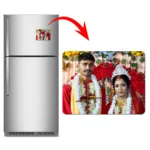 A product advertisement layout displaying a double-door grey refrigerator holding a horizontal rectangular custom flexible photo magnet. A red arrow leads to a larger widescreen view of the rectangle magnet, displaying a personalized Indian wedding photo of a bride and groom in traditional red outfits and floral garlands by upahar18.