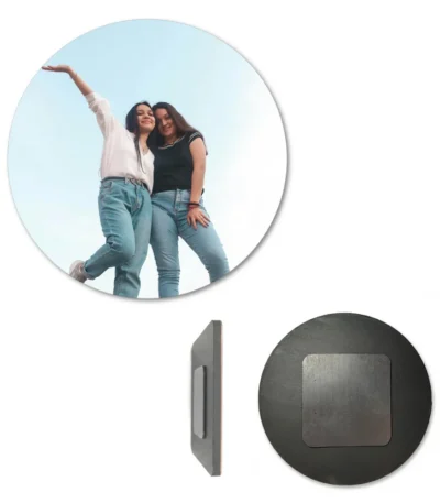 A circular round-shaped personalized MDF photo fridge magnet displayed alongside its side edge profile and its back face. The front circle shows a custom picture of two young women in jeans smiling and posing against a clear blue sky, while the back view displays a dark circular wooden surface with a square-shaped heavy-duty magnet attached by upahar18.